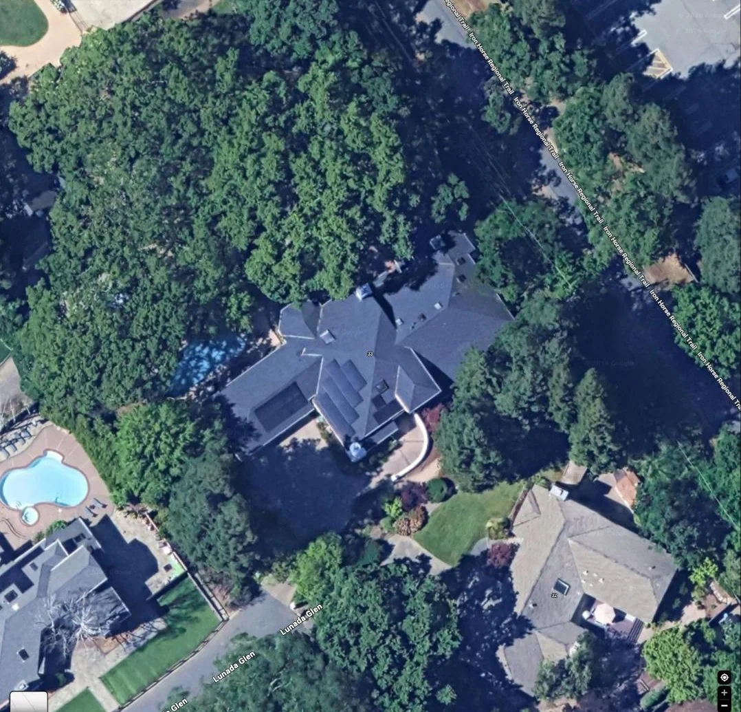 Aerial view of a wooded residential property with a large multi-gable rooftop and adjacent pool