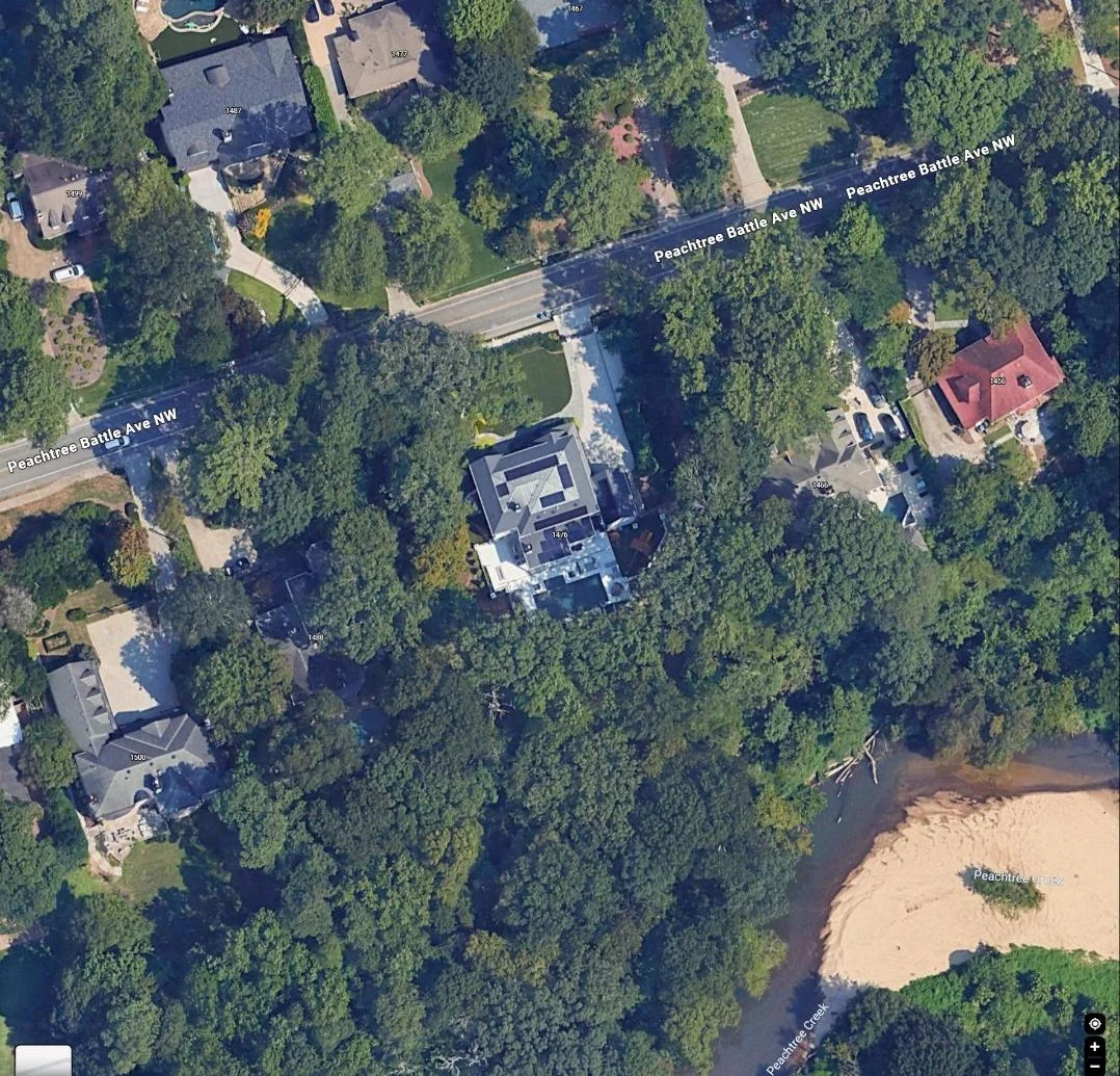 Aerial view of a wooded residential estate with a large multi-gable rooftop near a creek