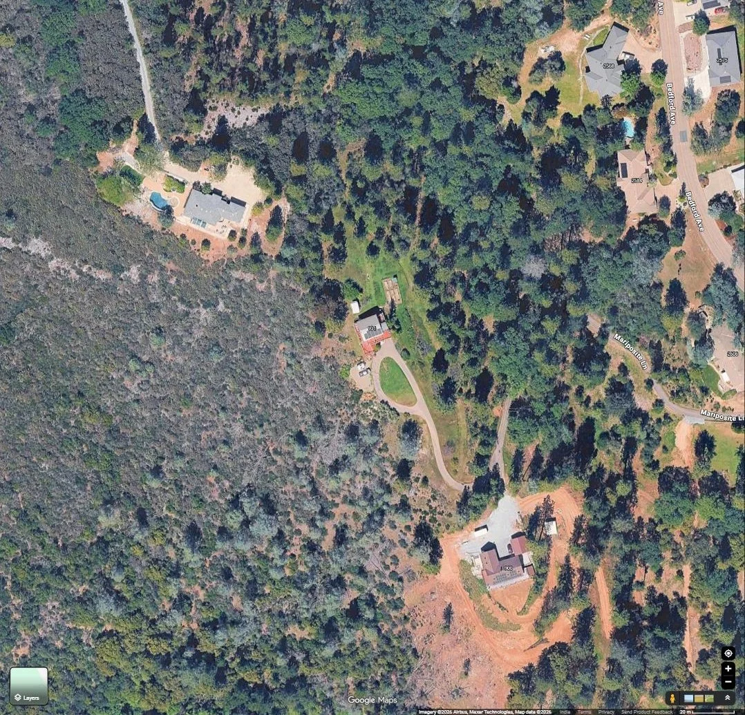 Aerial view of a wooded rural residential rooftop with a solar array, along a mountain road